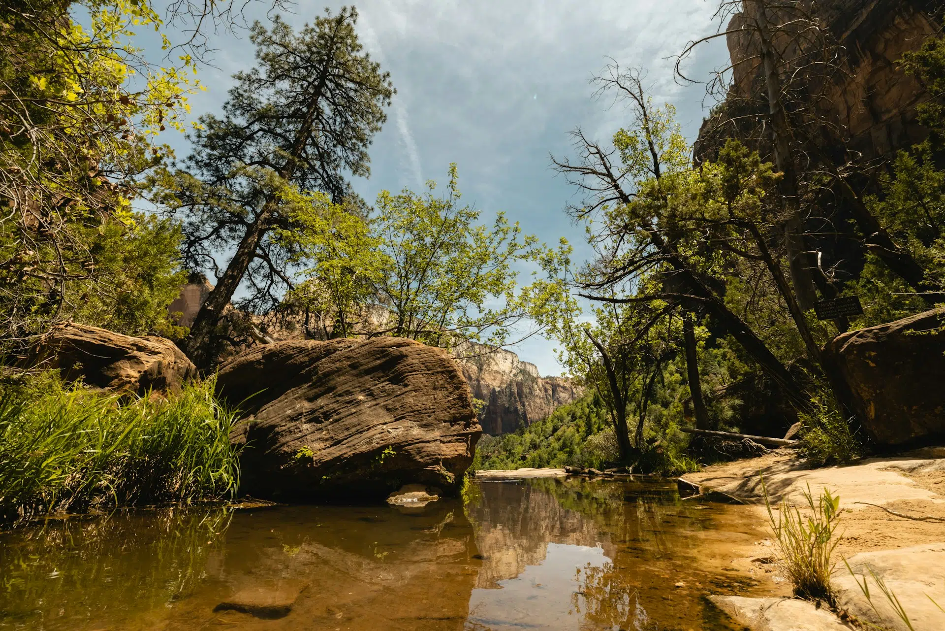 A tranquil river reflection surrounded by lush greenery and rocky cliffs under a clear sky.